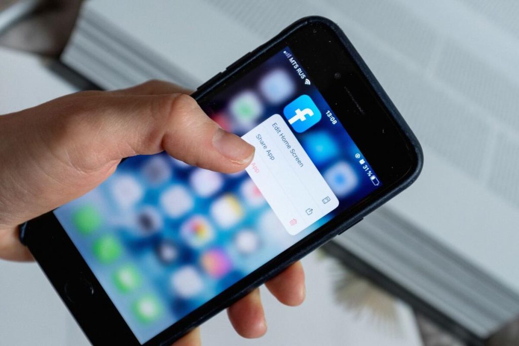 hand holding smartphone with social media app open, blurred feed, no faces visible